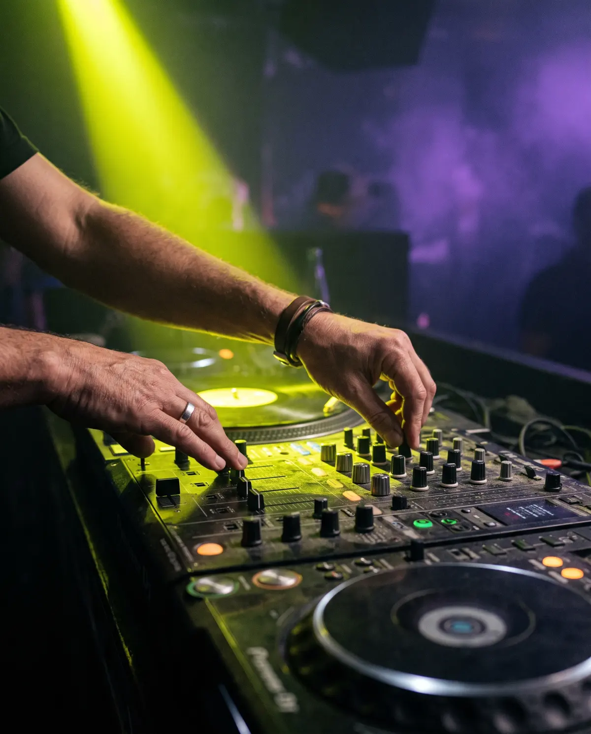 Mãos de DJ no mixer sob um spot amarelo ácido